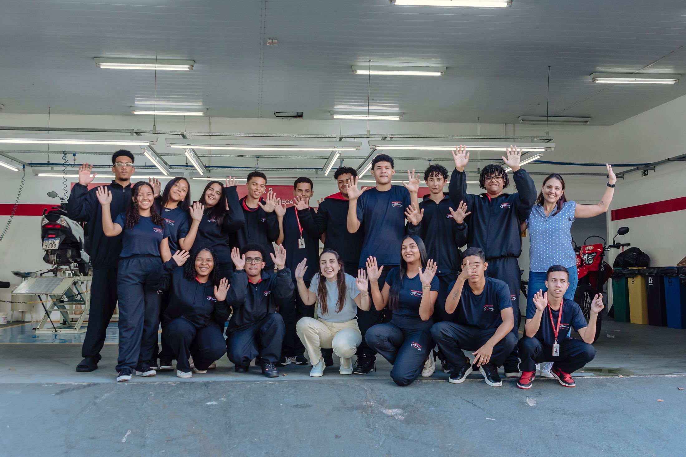 Turma de alunos e educadora acenando na oficina da Associação Beni Car